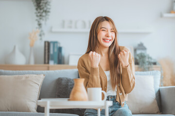 Ecstatic woman shout loud yeah fist up raise win lottery on sofa at home