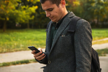 Fototapeta premium Young businessman using a phone outdoors in summer, technology and nature. Man in business attire using a smartphone outdoors in summer, nature background