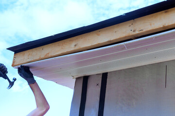 Worker installs plastic vinyl soffit on roof corner of rafters house