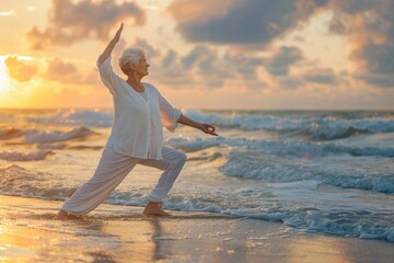 Fototapeta premium Senior Caucasian woman practicing yoga on the shore, performing a stretch in white clothes during a golden sunset.