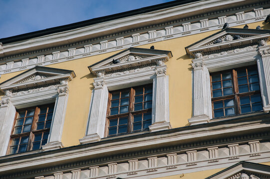 Three windows on the facade of a house with beige plaster in the central historical part of the city. Beautiful decorative architecture with reliefs, cornice and white columns in Lviv, Ukraine.