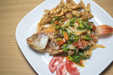 Indonesian food: fried nile tilapia (ikan nila goreng) with stir fried bok choy (sawi), crispy fried oyster mushroom (jamur tiram), and chopped tomatoes; on top of white rectangular plate