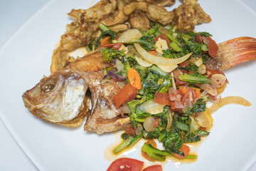 Indonesian food: fried nile tilapia (ikan nila goreng) with stir fried bok choy (sawi), crispy fried oyster mushroom (jamur tiram), and chopped tomatoes; on top of white rectangular plate