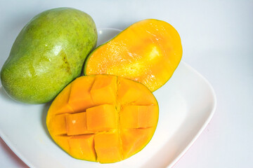 Two mangos, on a white tablecloth. One of them is cut open to show its inside, and one piece is diced.