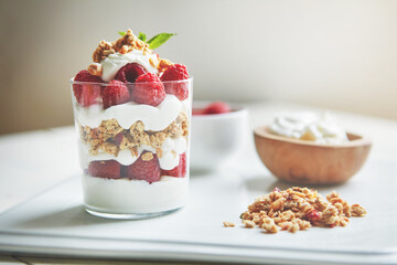 Breakfast, glass and yogurt with raspberry on plate for healthy food, vegan and cereal in morning. Vitamins, fruit and dairy in clear container with protein for weight loss, organic nutrition or diet