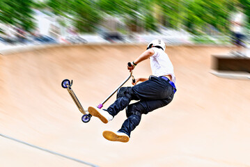 Young man practicing Scootering (Freestyle Scootering) in the new SkatePark in the central park of...