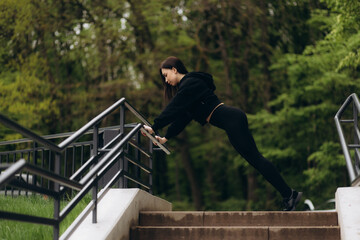 A teenager girl lunges while warming up and stretching her leg on the stairs before outdoor working...