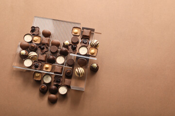 Heart made with delicious chocolate candies on brown background, top view. Space for text
