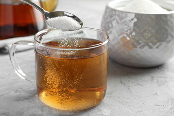 Adding sugar into cup of tea at grey textured table, closeup