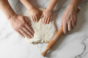 Father and child making dough at white table, top view