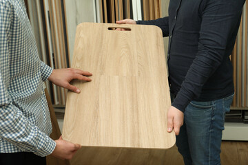 Men holding sample of wooden flooring in shop, closeup