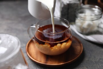 Pouring milk into cup of tea on grey table, closeup