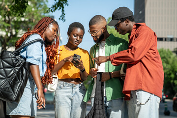 Black woman with phone shows friends video on Internet. Cheerful smiling African American students fellows walking outside after class, watching memes, blogs, posts, news on internet from smartphone
