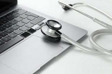 Modern laptop and stethoscope on white table, closeup