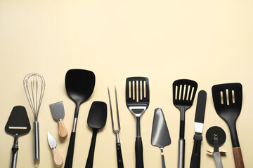 Different spatulas and other kitchen utensils on beige background, flat lay. Space for text