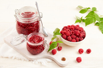 Homemade jam. Jars of raspberry jam and a bowl of fresh berries on a white wooden table 