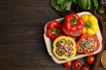 Quinoa stuffed bell peppers in baking dish, basil and tomatoes on wooden table, flat lay. Space for text