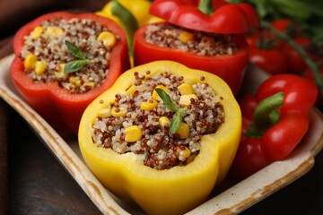 Quinoa stuffed bell peppers and basil in baking dish on wooden table, closeup