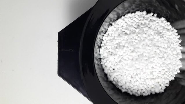 White masterbatch granules fall into a black measuring cup.Color pigment carrier polymer in the plastics industry