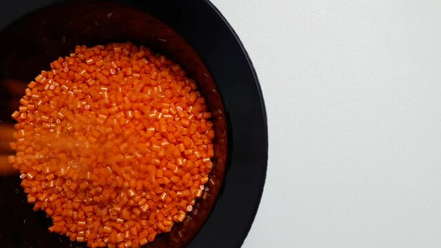 Orange masterbatch granules fall into a black measuring cup.Color pigment carrier polymer in the plastics industry