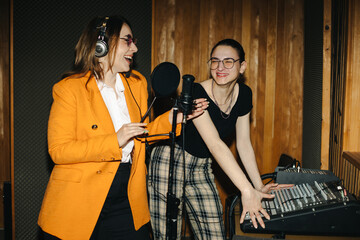 Smiling women in music studio. 
Producer and young woman musician creating music track in recording...