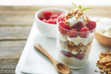 Glass, cereal and yogurt with raspberry with spoon for vegan food, organic or meal at breakfast. Fiber, dairy and fruit on plate by clear container with protein for morning, healthy nutrition or diet