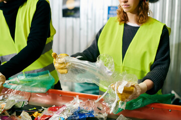 Young volunteers in gloves and safety vests are sorting trash together in a bin.