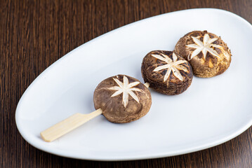 Three grilled and skewered mushrooms on a white plate.