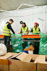 Young volunteers in gloves and safety vests work together to sort through boxes of trash at a table...