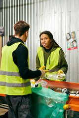 A man and a woman, in gloves and safety vests, standing in front of a table sorting trash as...