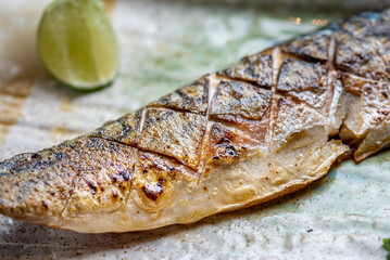 A close up of a grilled fish with a lime wedge on the side.
