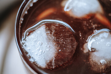 Close-up of glass cup with cold lemonade, cubes of ice, placed on table. Soft focus.