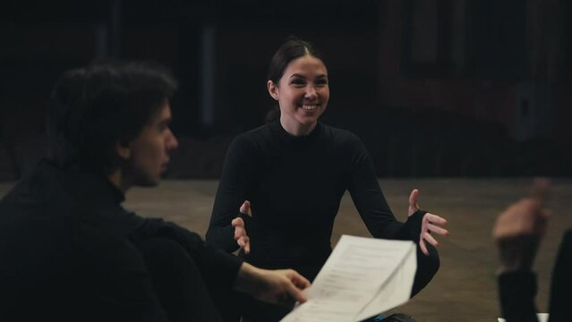 A happy brunette girl in a black suit an actress sits on stage and communicates with her colleagues during a rehearsal and preparation for a performance in the theater
