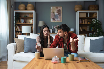 Young couple sitting at home using laptop computer having problem with credit card limit and...