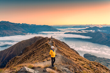 Asian hiker woman standing on the Roys Peak viewpoint with sunrise shine and fog on Wanaka at New...