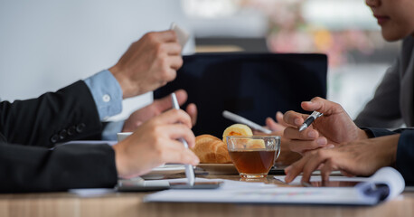 A group of people are having a meeting in an office. They are discussing some documents and drinking tea.