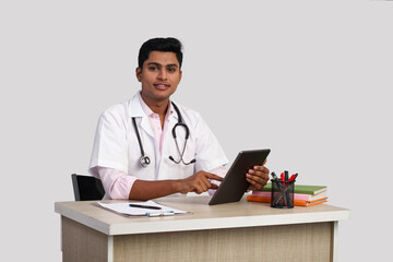 portrait of a young handsome Indian male doctor sitting at table using digital tablet 