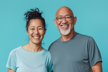 Fototapeta premium Portrait of a happy multicultural couple in their 50s wearing a moisture-wicking running shirt over pastel blue background