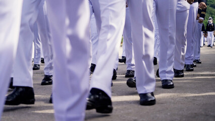 A group of cadets dressed in formal uniforms, marching in synchronized formation on a paved road...