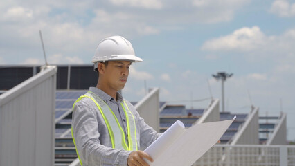 An engineer in a hard hat and safety vest reviews solar project plans on a tablet, standing at a site with solar panels.