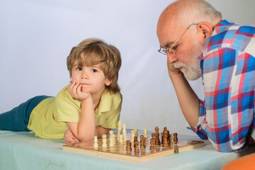 Chess competition. Little boy thinking about next move in game of chess. Board games. Grandfather and grandson playing chess. Child boy play chess with grandpa. Brain development and logic concept.