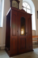 wooden cabinet with a glass door, placed in a room with a window. The confessional is a part of a church interior