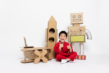 Asian little boy sitting with toy robot paper diy, cardboard airplane and rocket isolated on white...