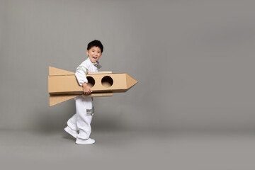 Asian little boy pilot or spaceman playing with cardboard rocket isolated on grey background, Kid...