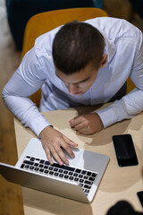 A young male office worker is deeply focused while working on a laptop at his desk, surrounded by a casual office environment.