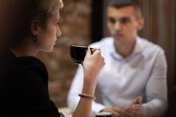 Focused business discussion at a modern cafe with a female professional drinking coffee while listening intently to her male colleague.