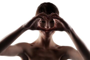 Silhouetted young woman forming heart shape with hands, expressing love