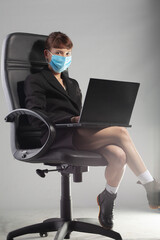 Young businesswoman with face mask working on laptop in office chair