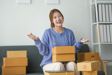Smiling woman with packages sitting on a couch in a home office. She looks happy and surprised with...