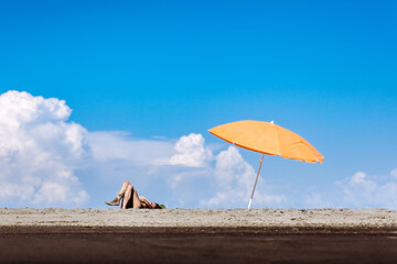 Young woman relaxing under an orange beach umbrella on a sunny day